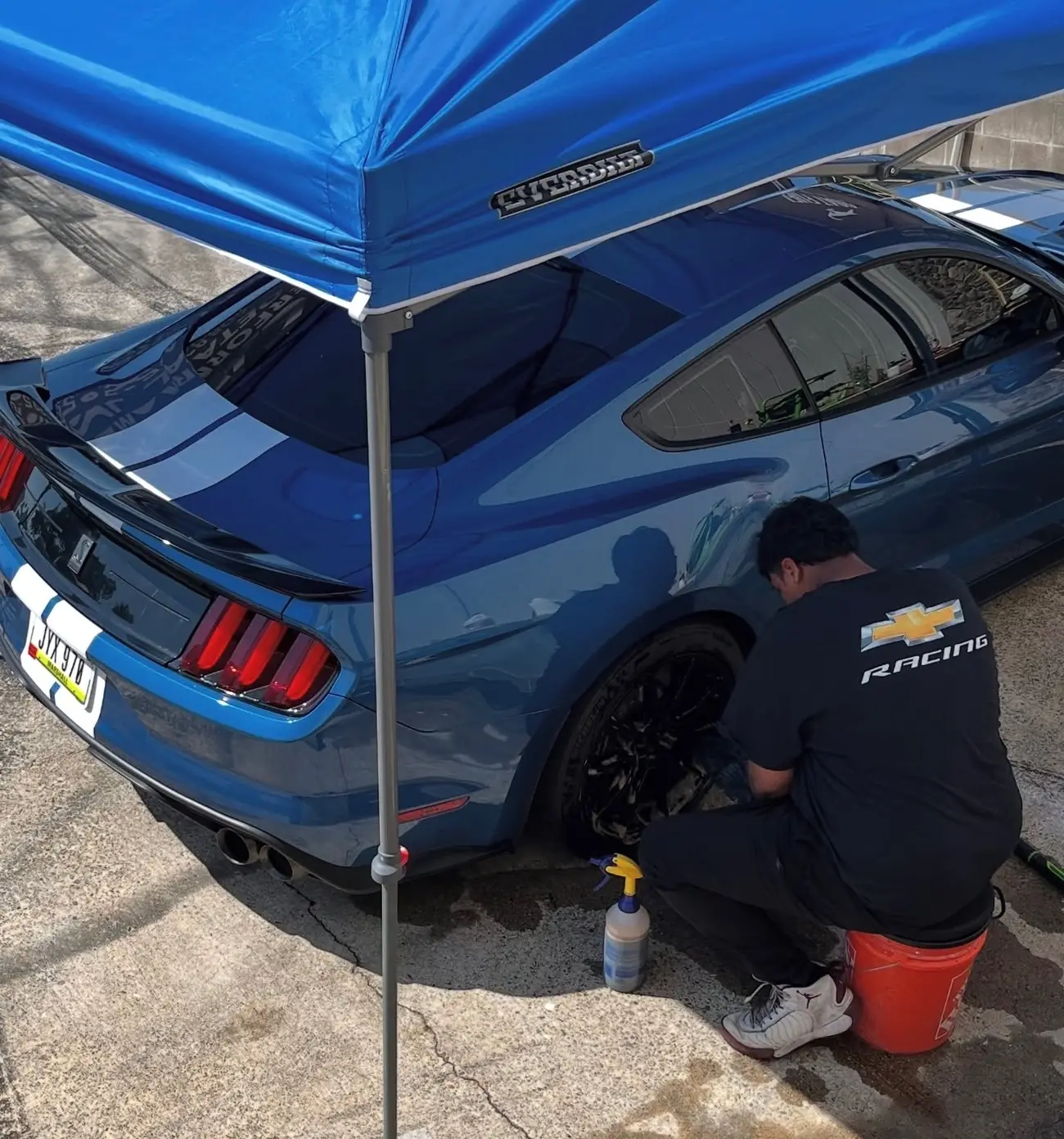 Detailer cleaning the wheel of a blue Shelby GT350 under a canopy